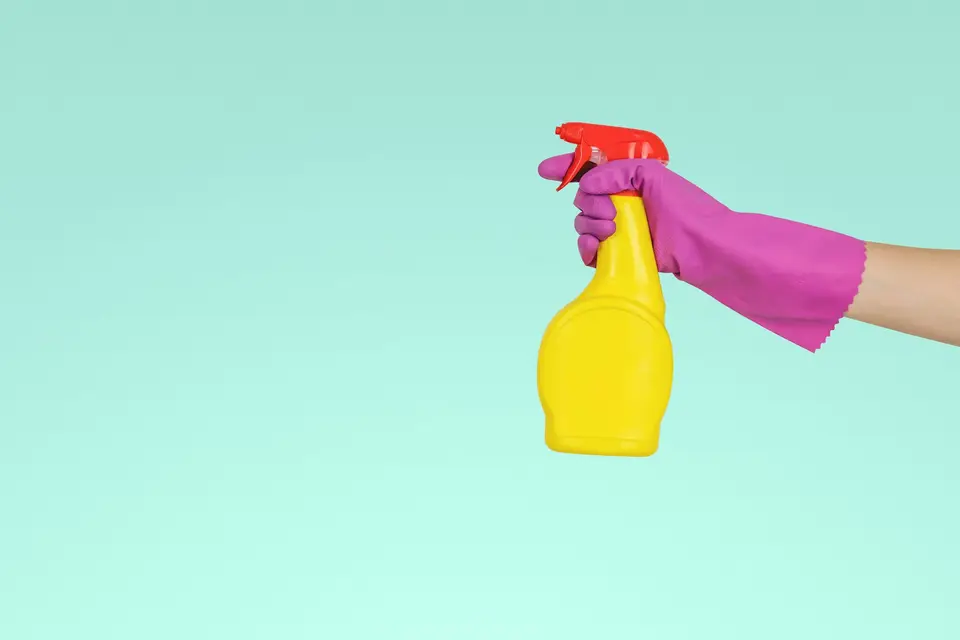 Hand in rubber glove holding a yellow spray bottle on a mint background
